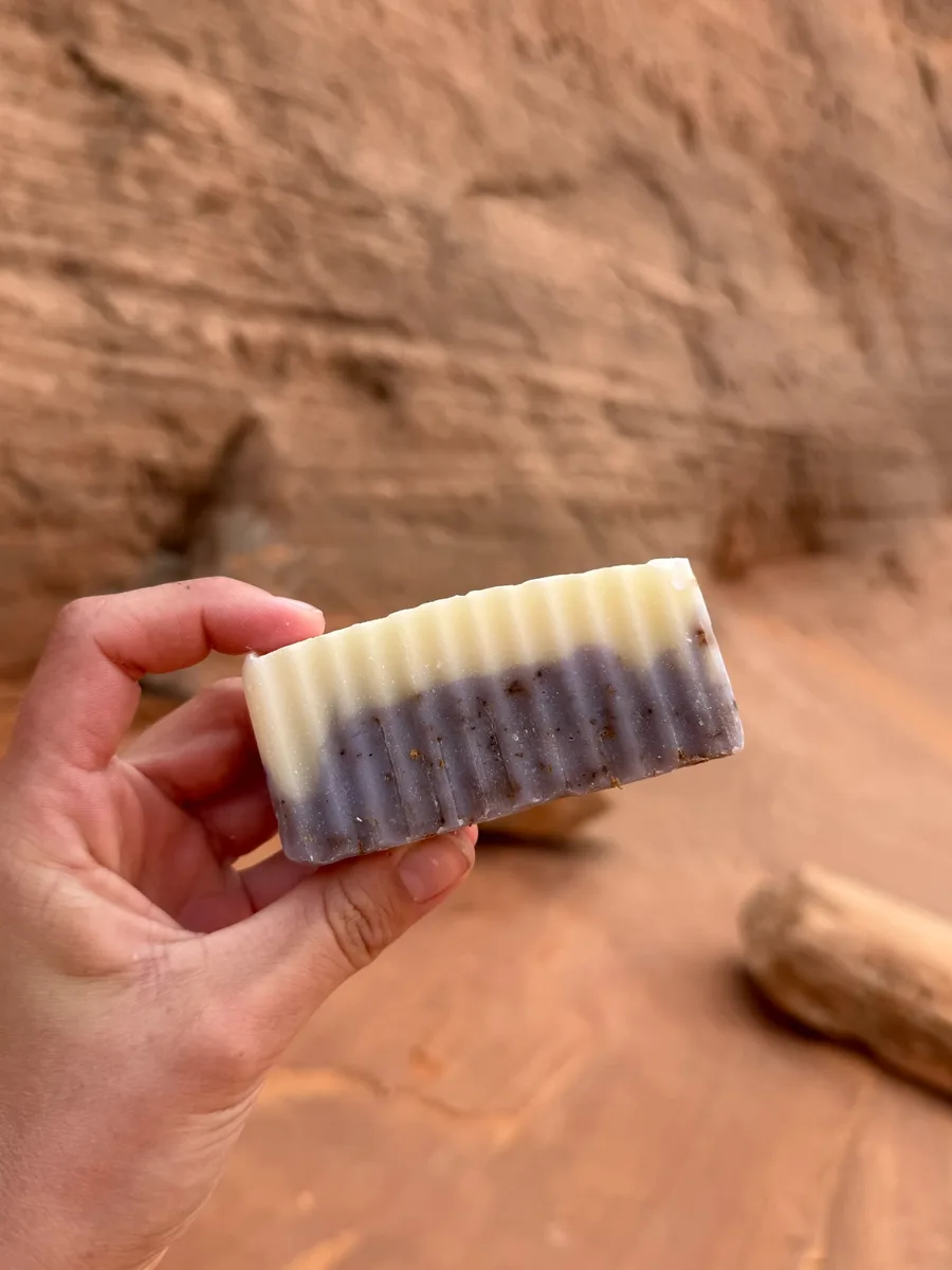 Handmade bar soap — two-tone lavender and cream, held against red sandstone