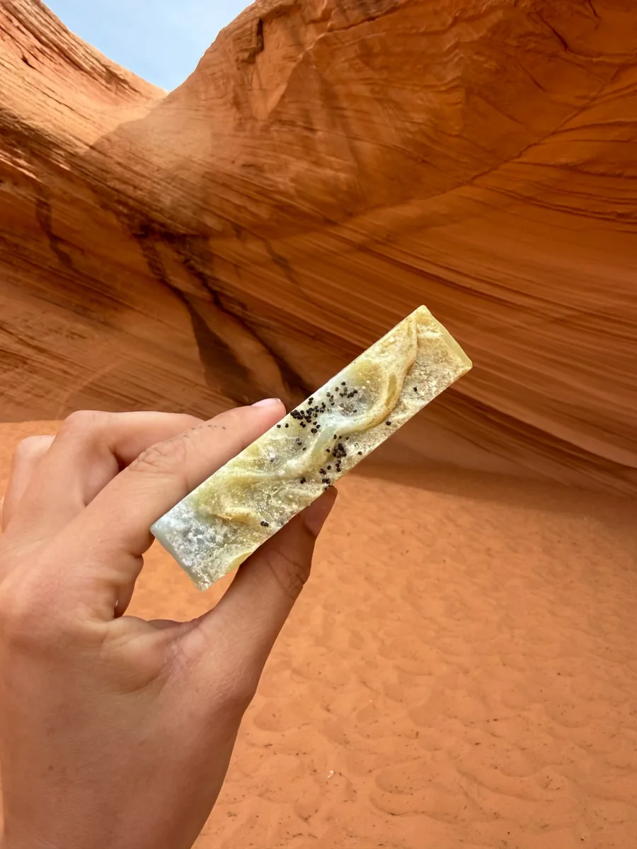 Handmade bar soap — golden with botanicals, held in a slot canyon